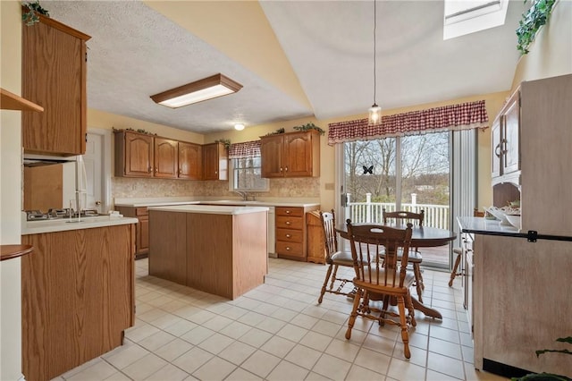 kitchen featuring pendant lighting, a center island, tasteful backsplash, light tile patterned flooring, and stainless steel gas stovetop