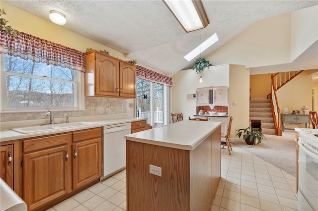 kitchen with sink, white appliances, a center island, vaulted ceiling with skylight, and light carpet