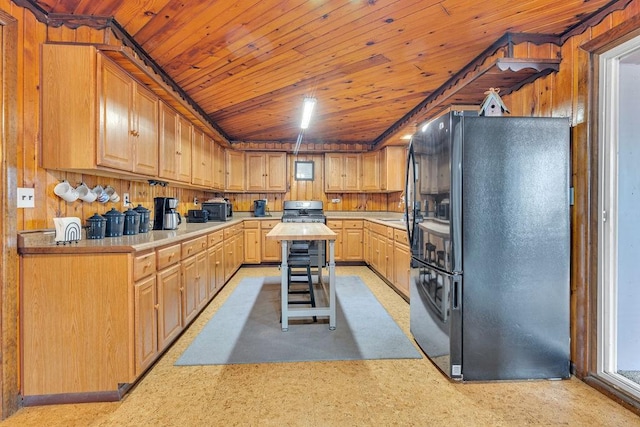 kitchen with black fridge, wooden walls, light brown cabinets, and wood ceiling