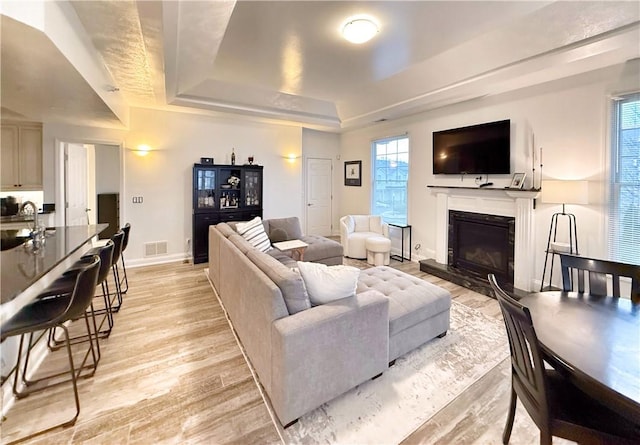 living room featuring a raised ceiling, sink, a wealth of natural light, and light wood-type flooring