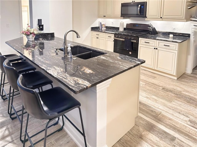 kitchen featuring sink, dark stone countertops, a breakfast bar area, gas stove, and cream cabinetry