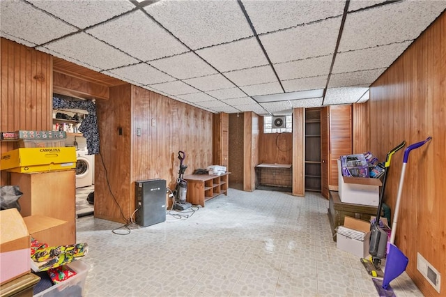 basement with wooden walls, washer / dryer, and a drop ceiling