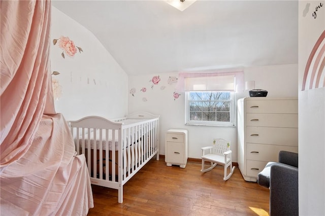 bedroom with hardwood / wood-style flooring, lofted ceiling, and a crib