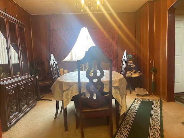 dining room with light colored carpet, a notable chandelier, and wooden walls