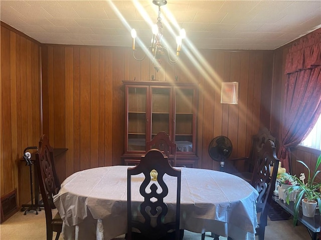 carpeted dining room featuring a chandelier and wood walls