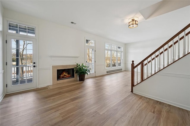 unfurnished living room featuring plenty of natural light, hardwood / wood-style floors, and baseboard heating