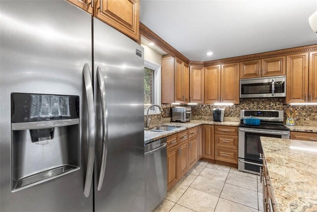 kitchen with sink, light stone counters, light tile patterned floors, stainless steel appliances, and backsplash