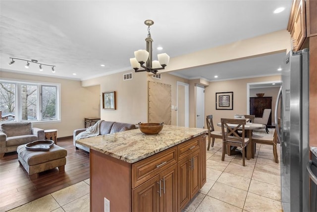 kitchen with pendant lighting, stainless steel fridge, light stone counters, ornamental molding, and a chandelier