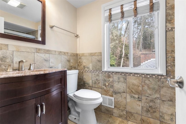 bathroom featuring vanity, a healthy amount of sunlight, tile walls, and toilet