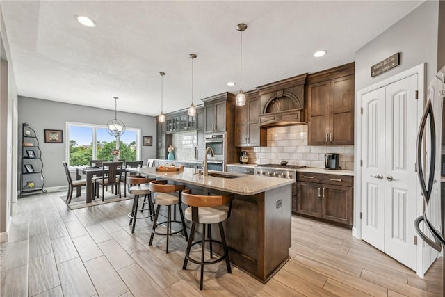 kitchen with dark brown cabinetry, decorative light fixtures, sink, and a center island with sink