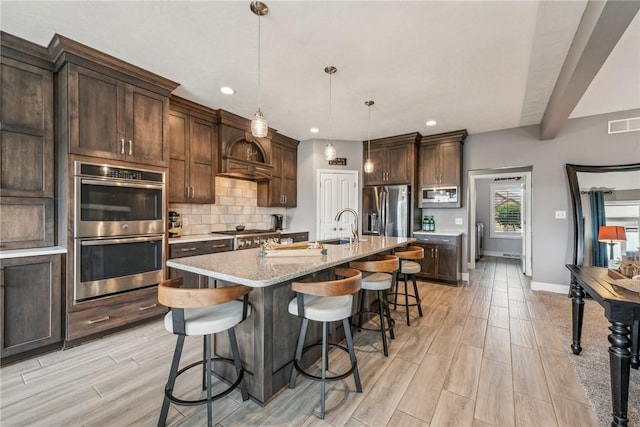 kitchen with pendant lighting, stainless steel appliances, tasteful backsplash, light stone countertops, and a center island with sink