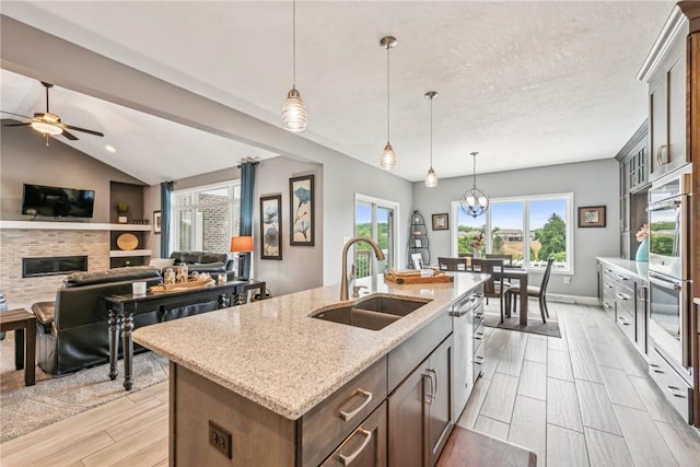 kitchen with sink, light stone counters, decorative light fixtures, a brick fireplace, and a kitchen island with sink