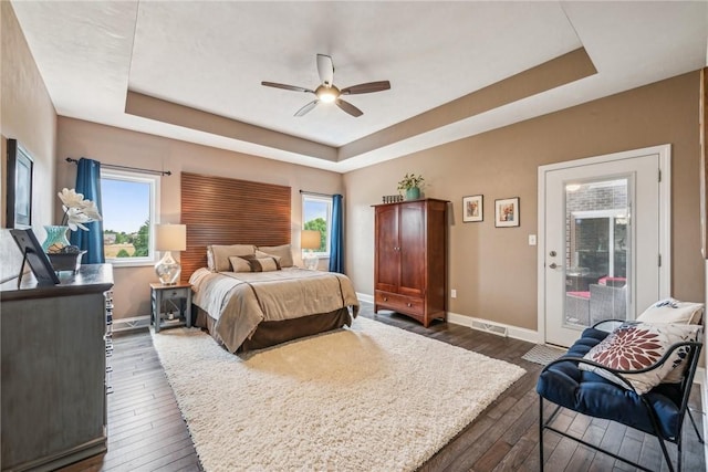 bedroom with ceiling fan, dark hardwood / wood-style flooring, and a raised ceiling