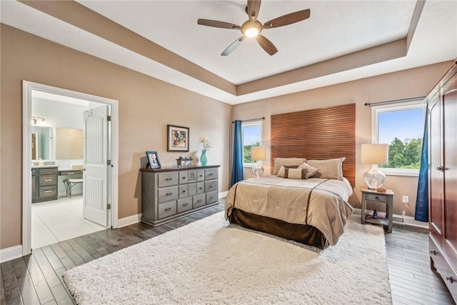 bedroom featuring ceiling fan, connected bathroom, a tray ceiling, and dark hardwood / wood-style flooring