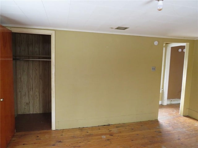 unfurnished bedroom with wood-type flooring, crown molding, and a closet