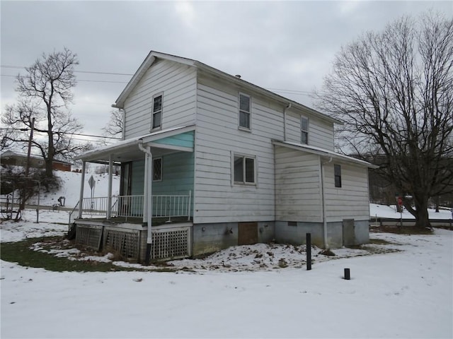 snow covered back of property featuring covered porch