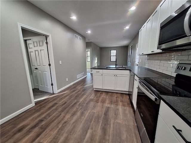 kitchen featuring dark wood-type flooring, appliances with stainless steel finishes, tasteful backsplash, white cabinets, and kitchen peninsula