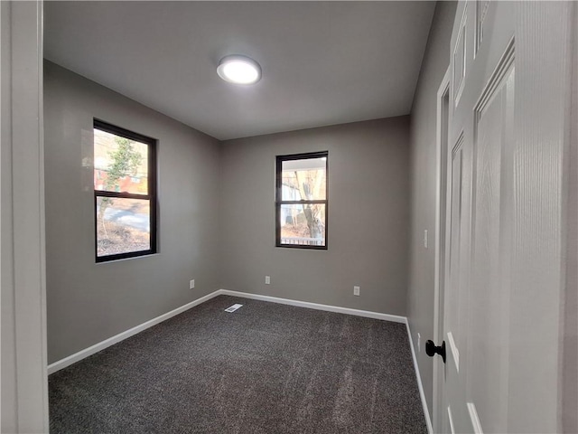 spare room featuring plenty of natural light and dark carpet