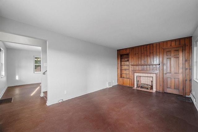 unfurnished living room with a tile fireplace, wooden walls, and built in shelves