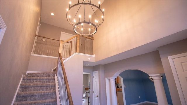 stairway featuring a towering ceiling, a chandelier, and decorative columns