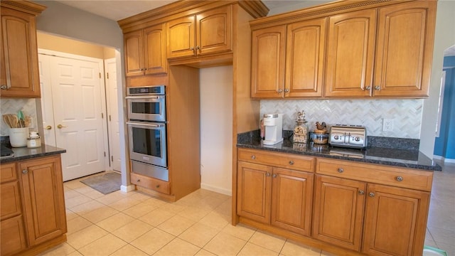 kitchen featuring dark stone countertops, backsplash, double oven, and light tile patterned floors