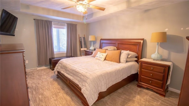 carpeted bedroom with a raised ceiling and ceiling fan