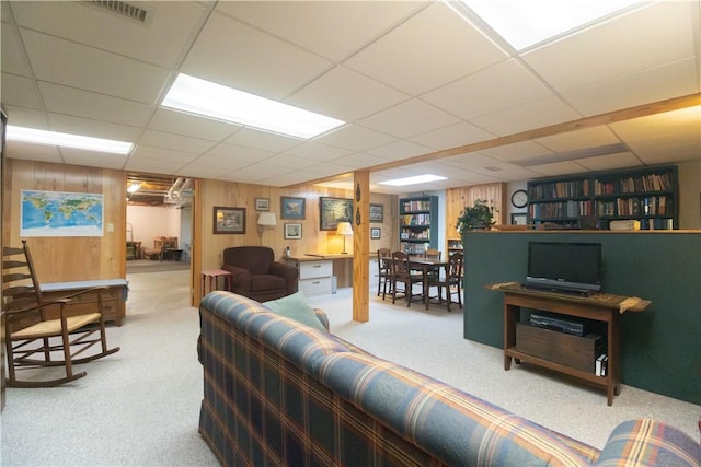 carpeted living room featuring wooden walls and a paneled ceiling