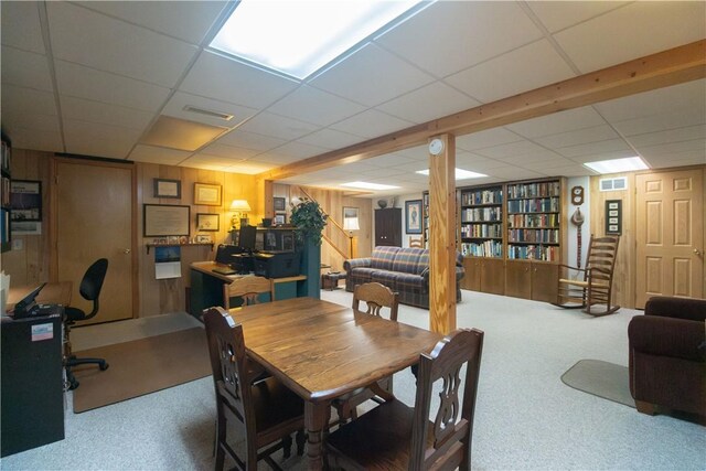 carpeted dining space with wooden walls and a paneled ceiling