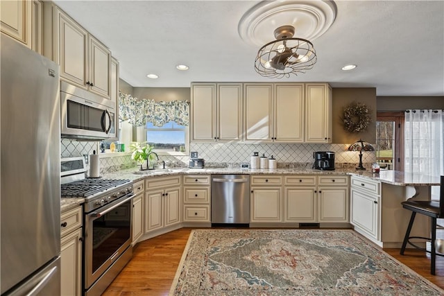 kitchen featuring sink, light stone counters, cream cabinetry, stainless steel appliances, and light hardwood / wood-style flooring