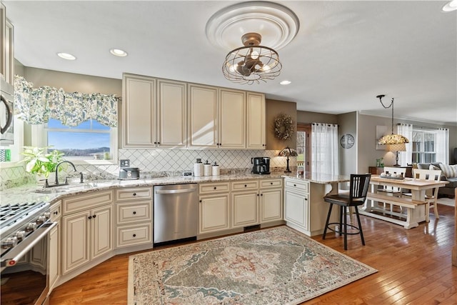 kitchen featuring pendant lighting, stainless steel appliances, light hardwood / wood-style flooring, and cream cabinetry