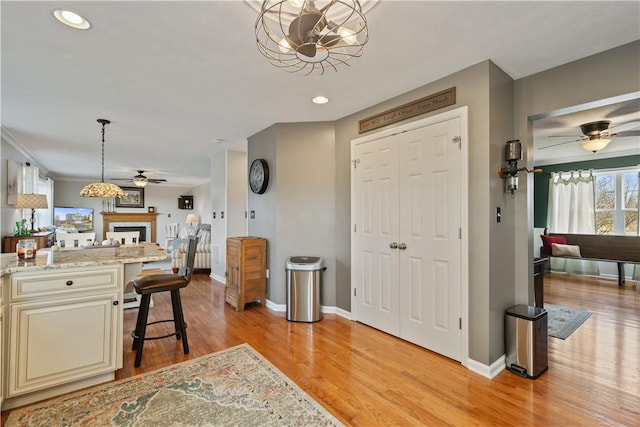 interior space featuring light hardwood / wood-style flooring, light stone counters, cream cabinets, a kitchen bar, and decorative light fixtures