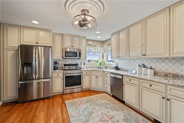 kitchen with pendant lighting, sink, cream cabinetry, stainless steel appliances, and light hardwood / wood-style flooring