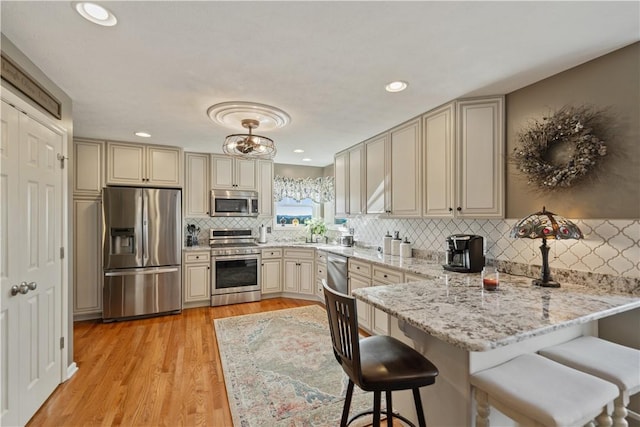 kitchen featuring appliances with stainless steel finishes, light stone counters, kitchen peninsula, a kitchen bar, and cream cabinetry