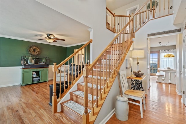 staircase with crown molding, ceiling fan, wood-type flooring, and a high ceiling