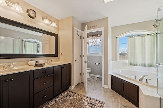 bathroom featuring tiled tub, vanity, tile patterned floors, and toilet