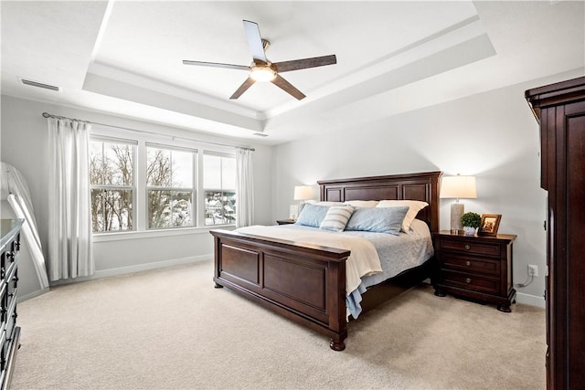 bedroom with a raised ceiling, visible vents, light carpet, ceiling fan, and baseboards