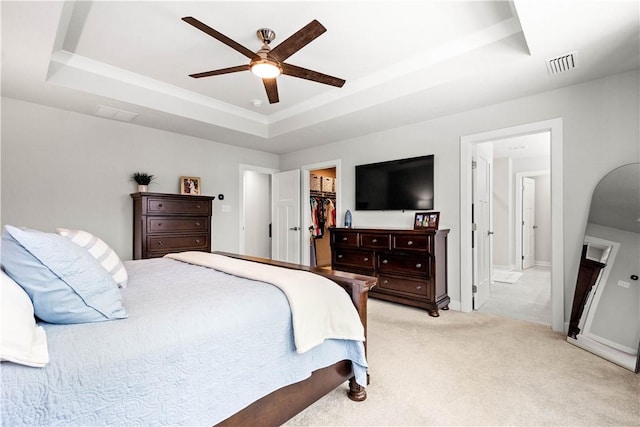 bedroom with a spacious closet, visible vents, a raised ceiling, and light colored carpet