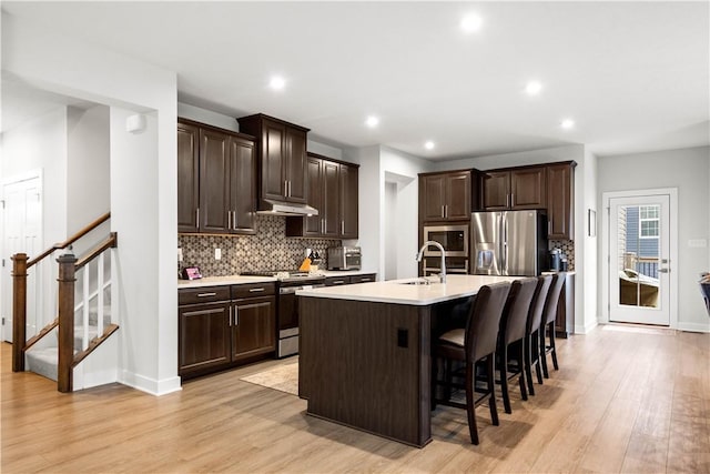 kitchen with stainless steel appliances, dark brown cabinets, light countertops, under cabinet range hood, and a sink