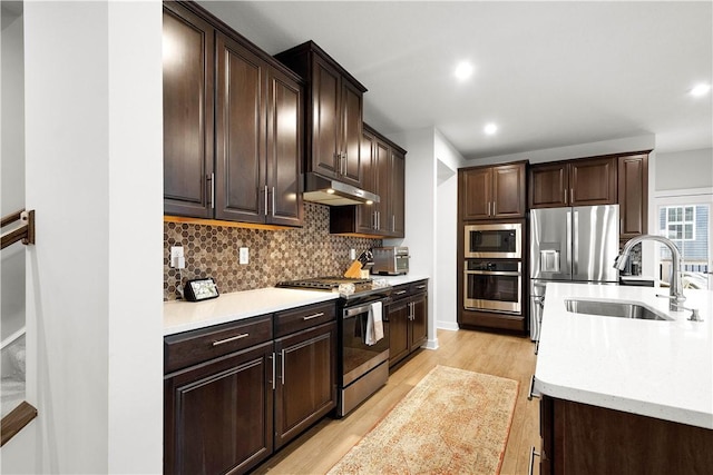 kitchen featuring stainless steel appliances, light countertops, a sink, and under cabinet range hood