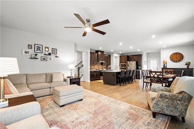 living room with stairs, recessed lighting, a ceiling fan, and light wood-style floors