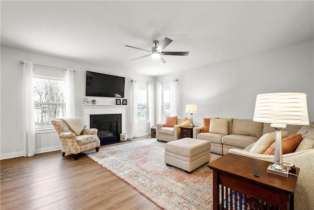 living room featuring a fireplace with flush hearth, wood finished floors, a ceiling fan, and baseboards