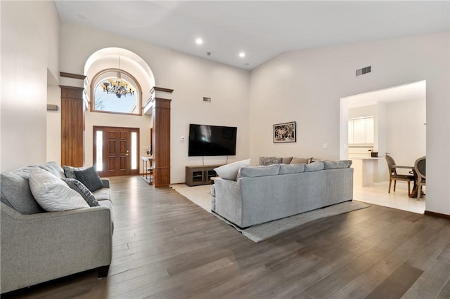 living room featuring dark wood-type flooring, high vaulted ceiling, decorative columns, and a notable chandelier