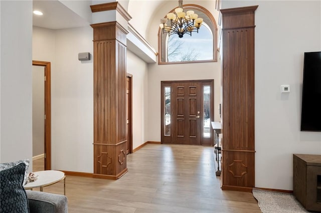 foyer with decorative columns, a towering ceiling, an inviting chandelier, and light wood-type flooring