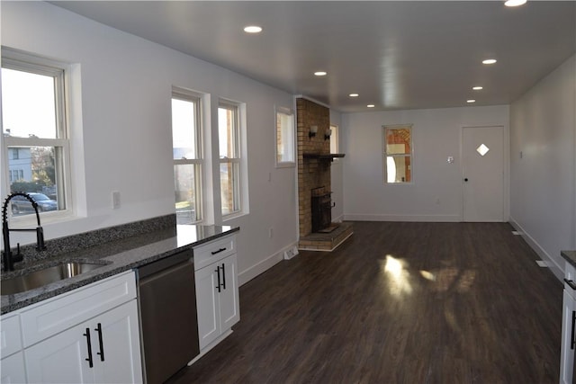 kitchen featuring sink, white cabinetry, stainless steel dishwasher, dark stone counters, and a fireplace