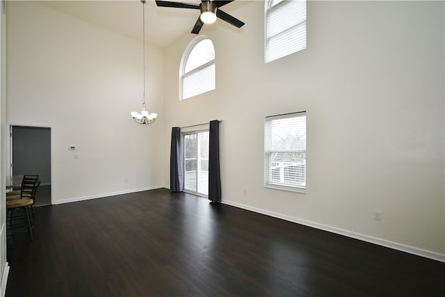 unfurnished living room featuring a towering ceiling, plenty of natural light, dark hardwood / wood-style flooring, and ceiling fan with notable chandelier