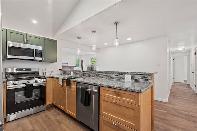 kitchen with appliances with stainless steel finishes, dark hardwood / wood-style flooring, kitchen peninsula, stone counters, and pendant lighting