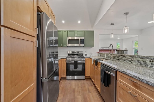 kitchen with decorative light fixtures, green cabinetry, stainless steel appliances, light stone countertops, and light wood-type flooring