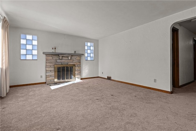 unfurnished living room featuring plenty of natural light, a stone fireplace, and carpet