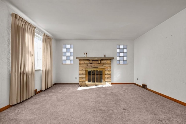 unfurnished living room with a stone fireplace, carpet floors, and a wealth of natural light