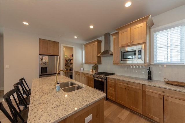 kitchen with wall chimney range hood, a breakfast bar area, an island with sink, and appliances with stainless steel finishes